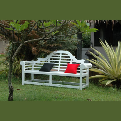 White garden bench with black and red cushions in a grassy area with plants.