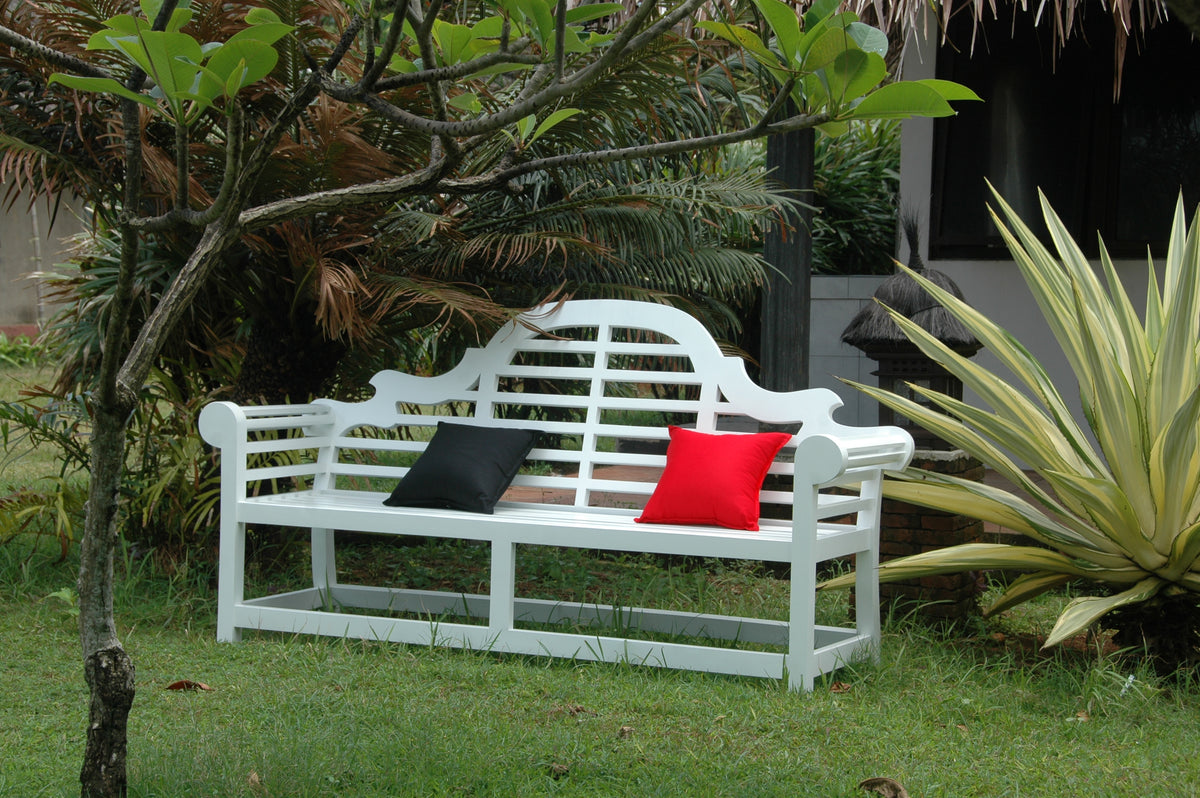 White garden bench with black and red cushions in a grassy area with plants.