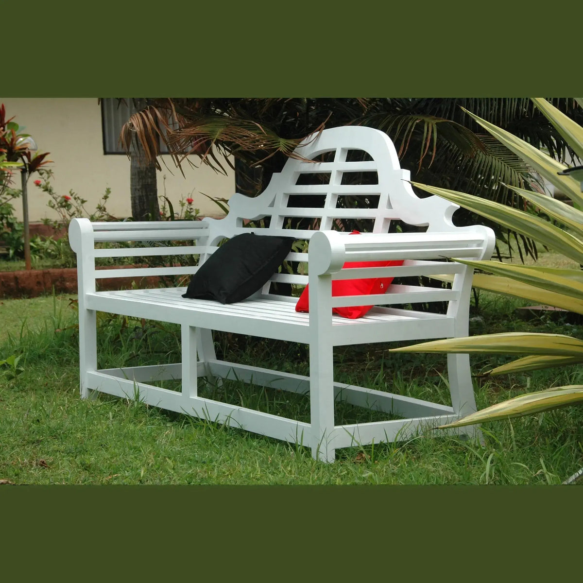 White garden bench with a black bag and red container on grass, surrounded by plants