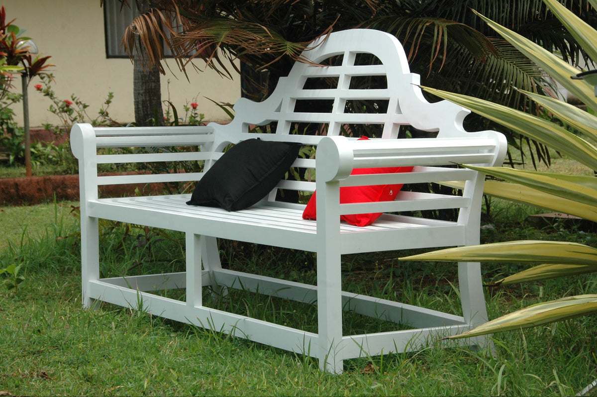White garden bench with a black bag and red container on grass, surrounded by plants