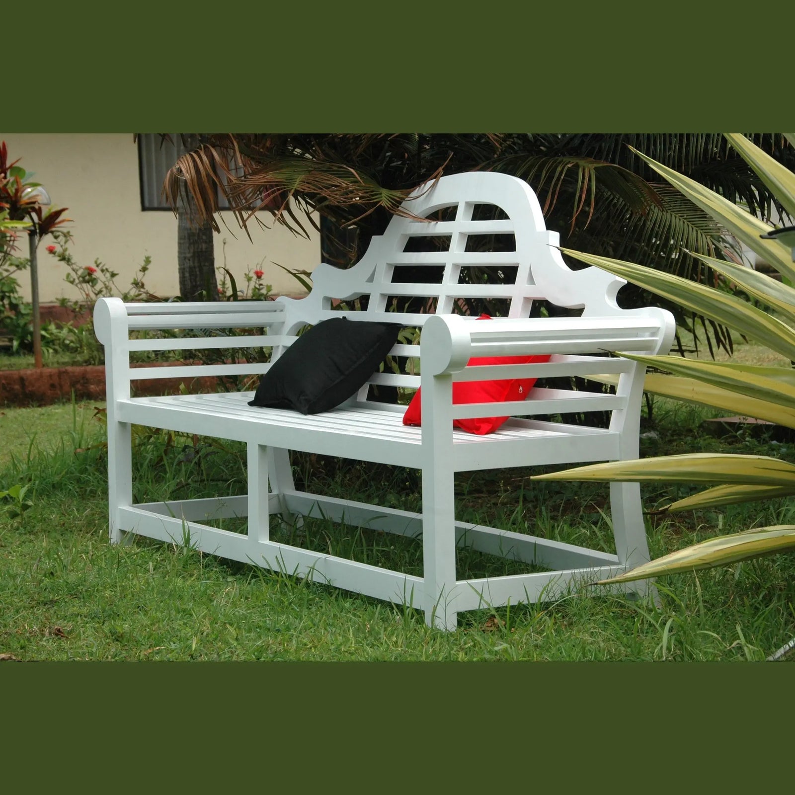 White garden bench with a black bag and red container on grass, surrounded by plants