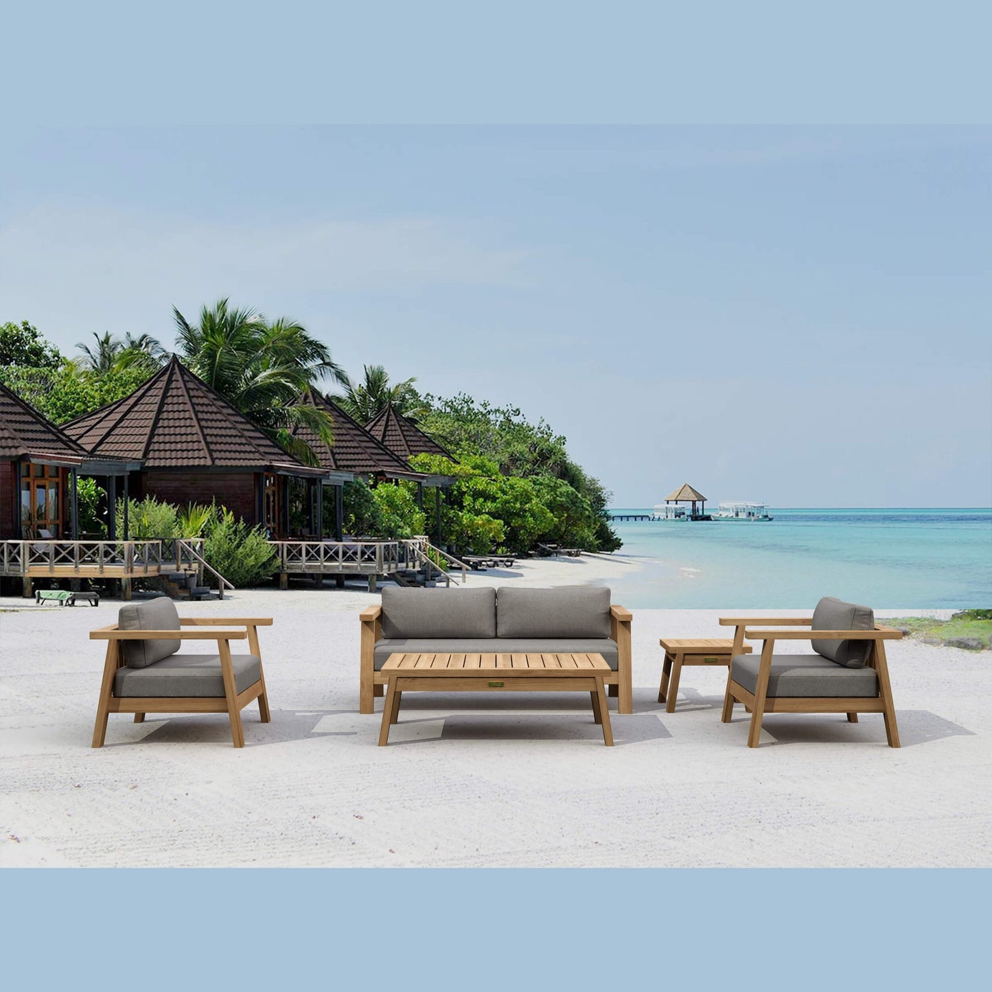 Outdoor furniture set on a sandy beach with ocean and tropical trees in the background