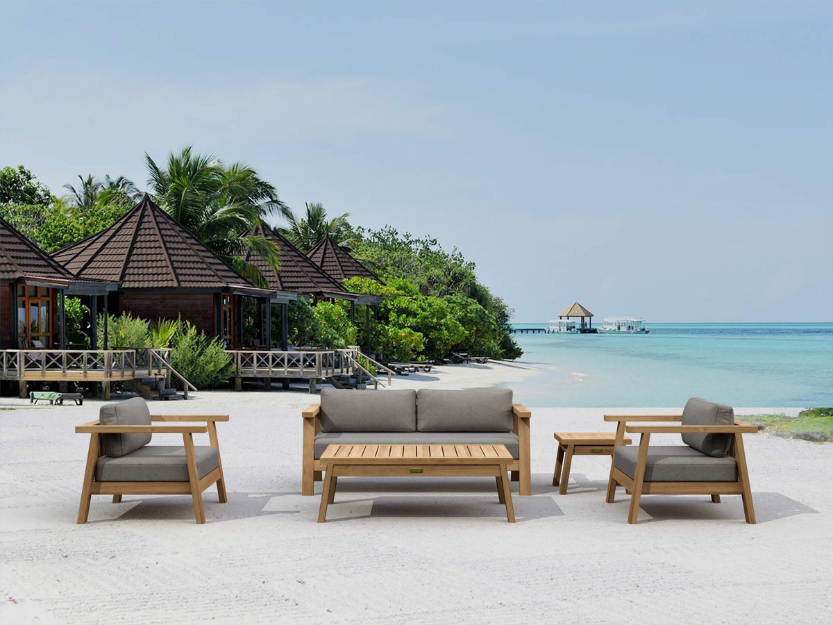 Outdoor furniture set on a sandy beach with ocean and tropical trees in the background