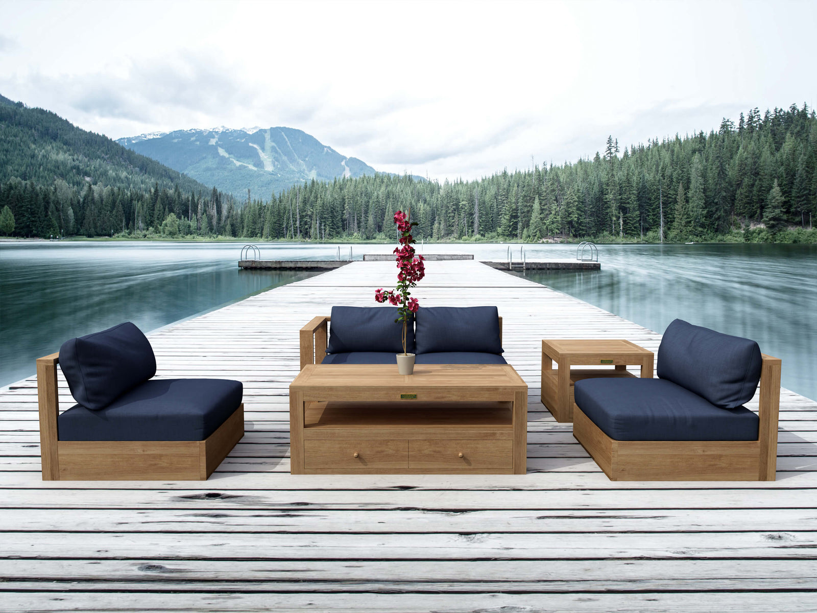 Outdoor wooden furniture set with blue cushions on a dock by a lake with mountains in the background