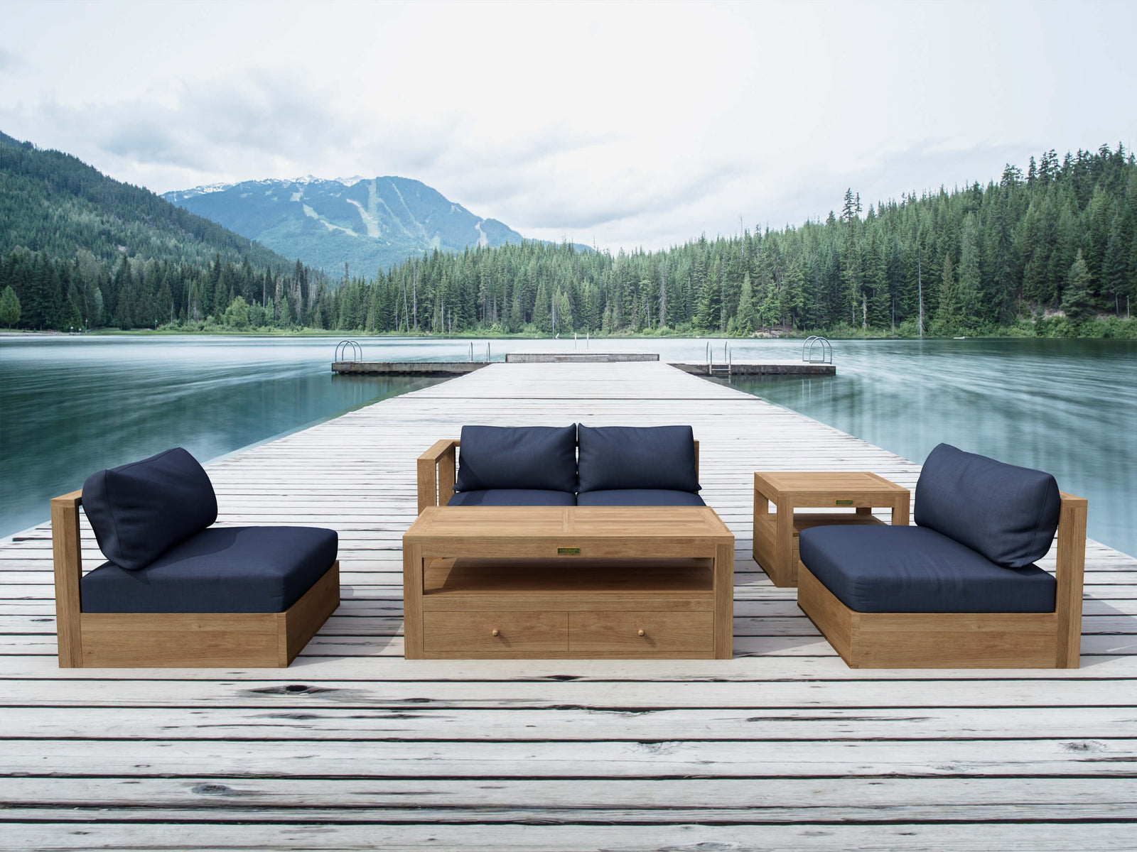 Outdoor wooden furniture set with blue cushions on a dock by a lake with mountains in the background