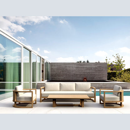 Outdoor patio set with sofa, chairs, and coffee table on a modern patio with pool and glass walls.
