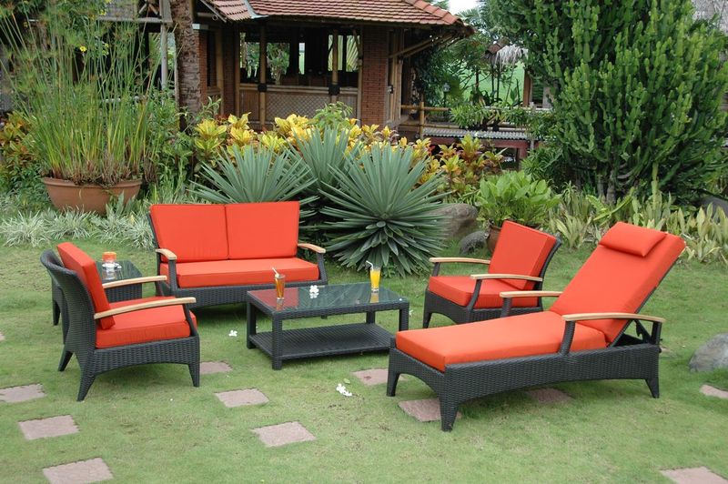 Outdoor patio set with red cushions on a grassy area with plants and a gazebo in the background.