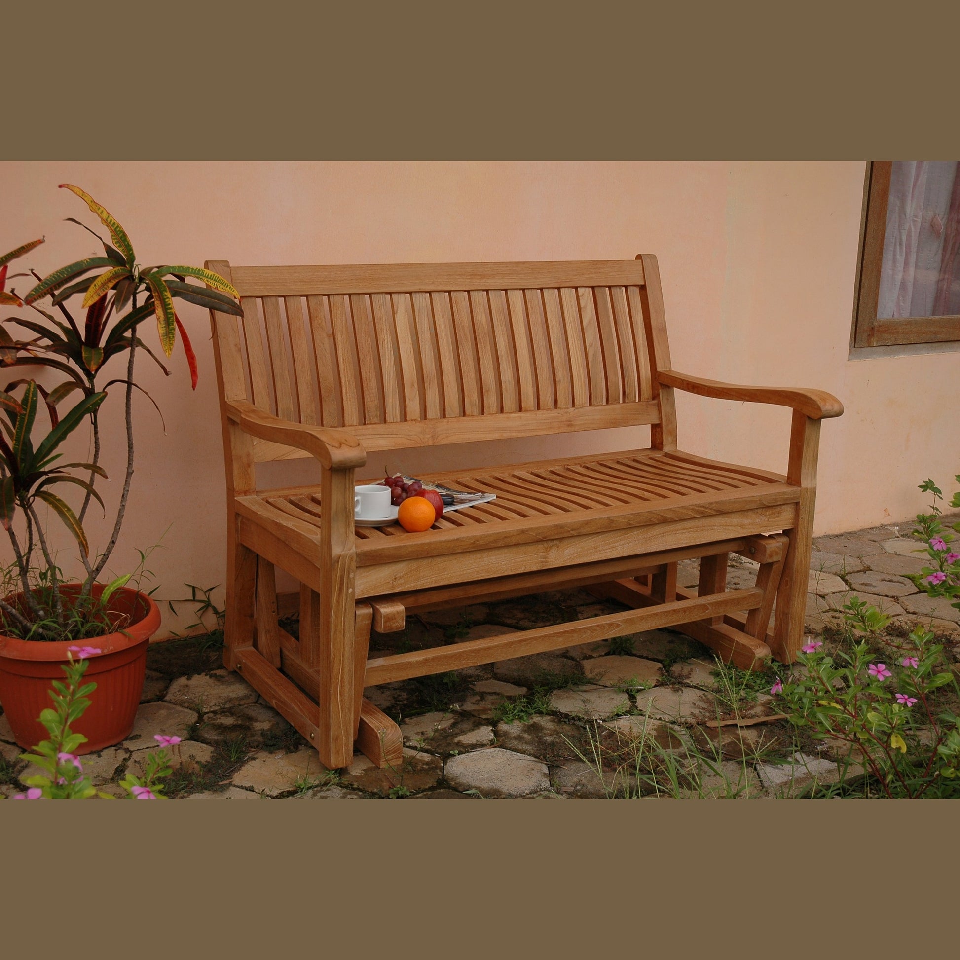 Wooden bench outdoors with a potted plant and flowers in the foreground.