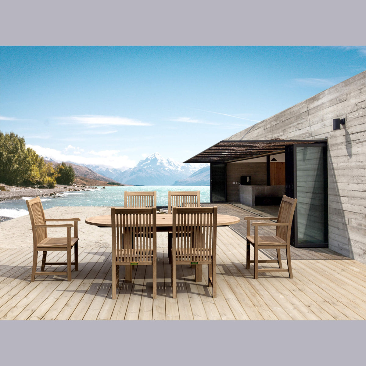Outdoor dining area with wooden table and chairs on a deck overlooking a scenic lake and mountains.