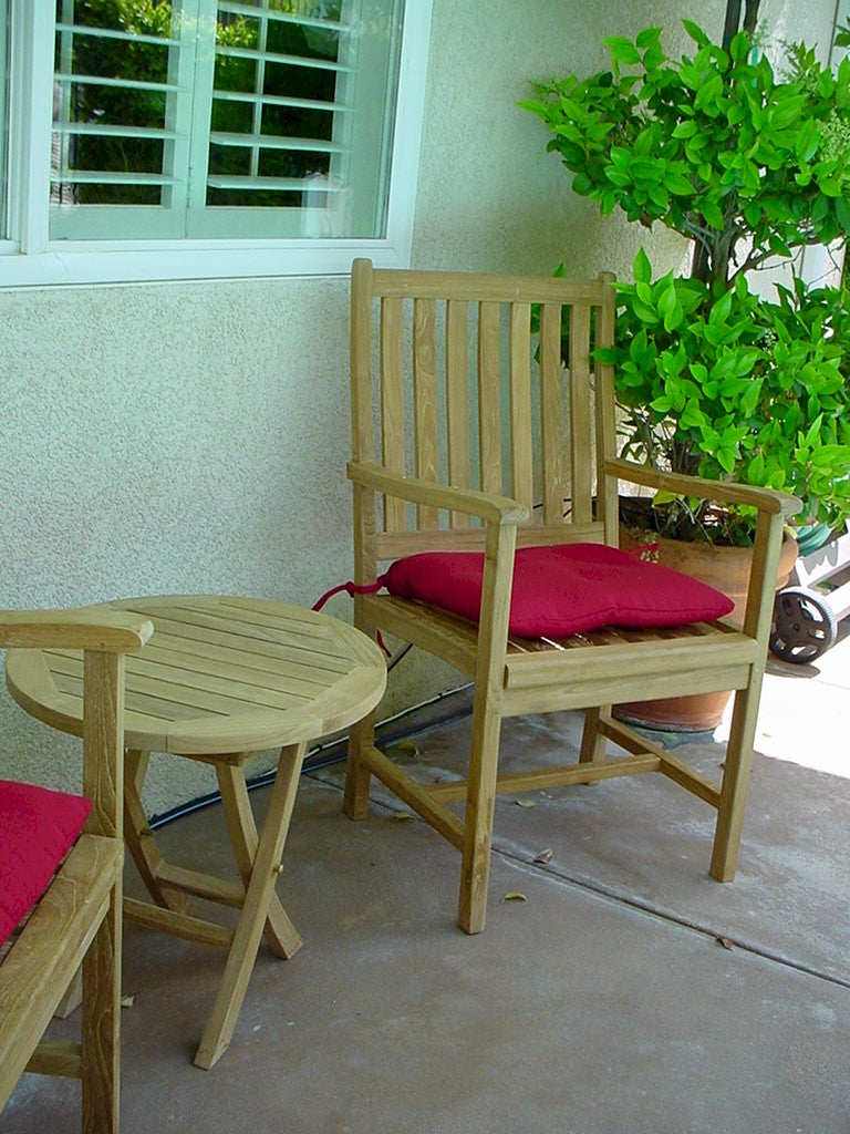 Wooden chair with a red cushion on a patio next to a small round table.