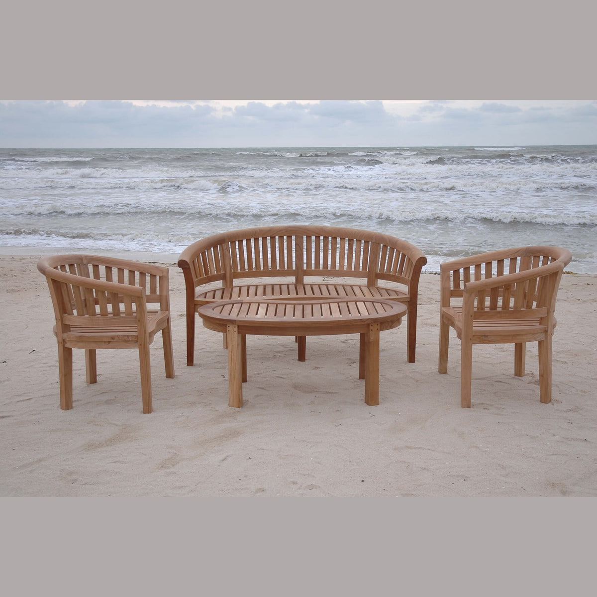 Wooden outdoor furniture set on a sandy beach with ocean waves in the background
