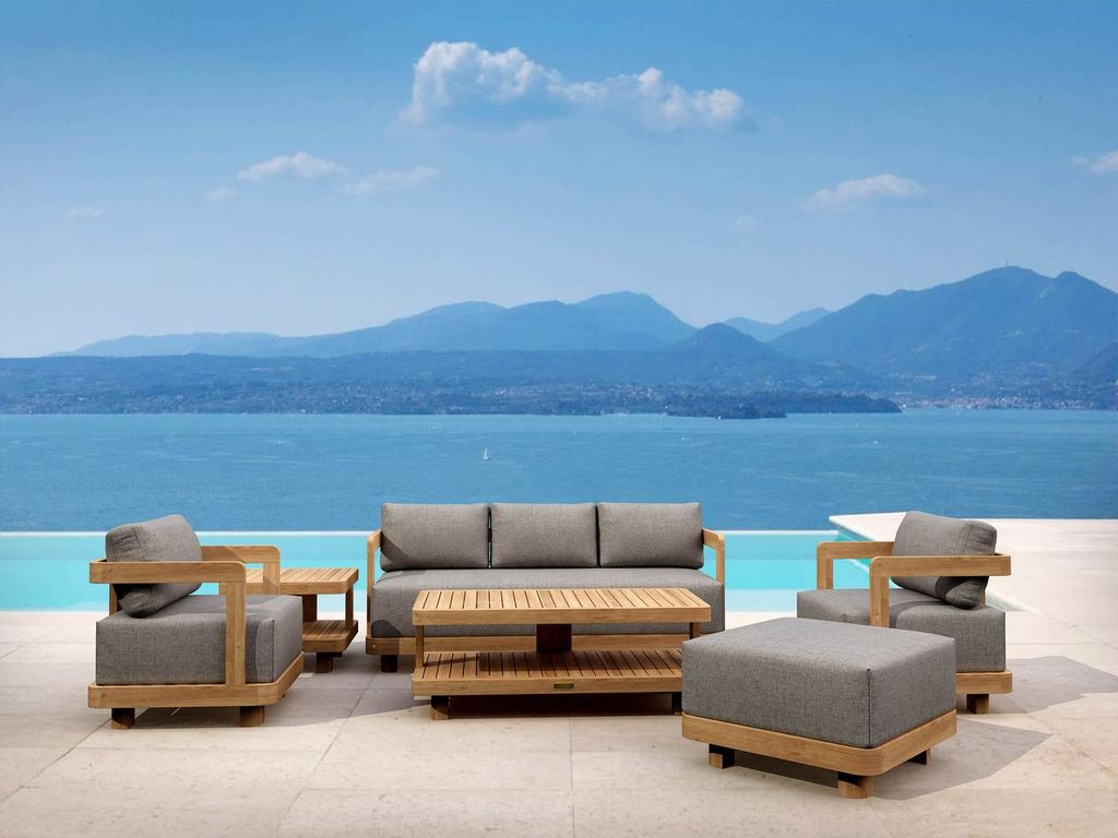 Outdoor furniture set with gray cushions and wooden frames by a scenic waterfront.