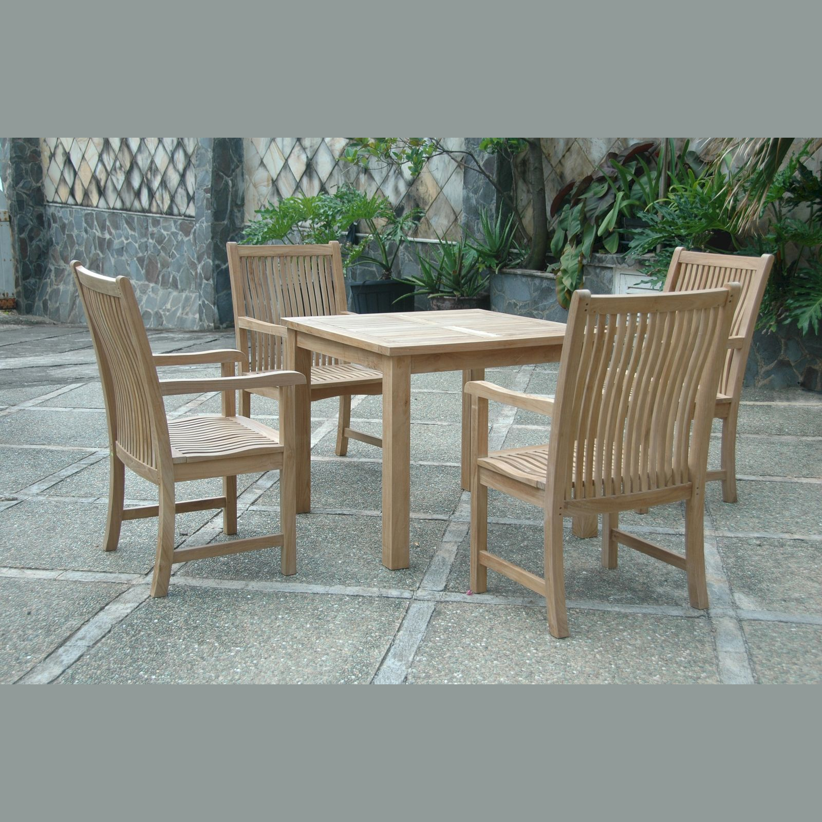 Outdoor teak furniture set with a table and four chairs on a stone patio.