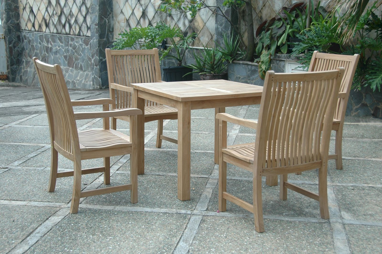 Outdoor teak furniture set with a table and four chairs on a stone patio.