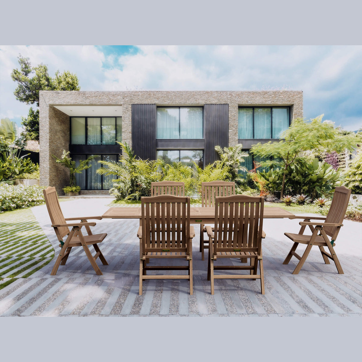 Wooden outdoor dining set on a patio with a modern house and garden in the background