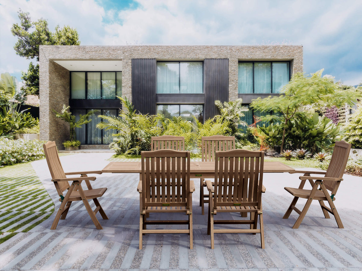 Wooden outdoor dining set on a patio with a modern house and garden in the background