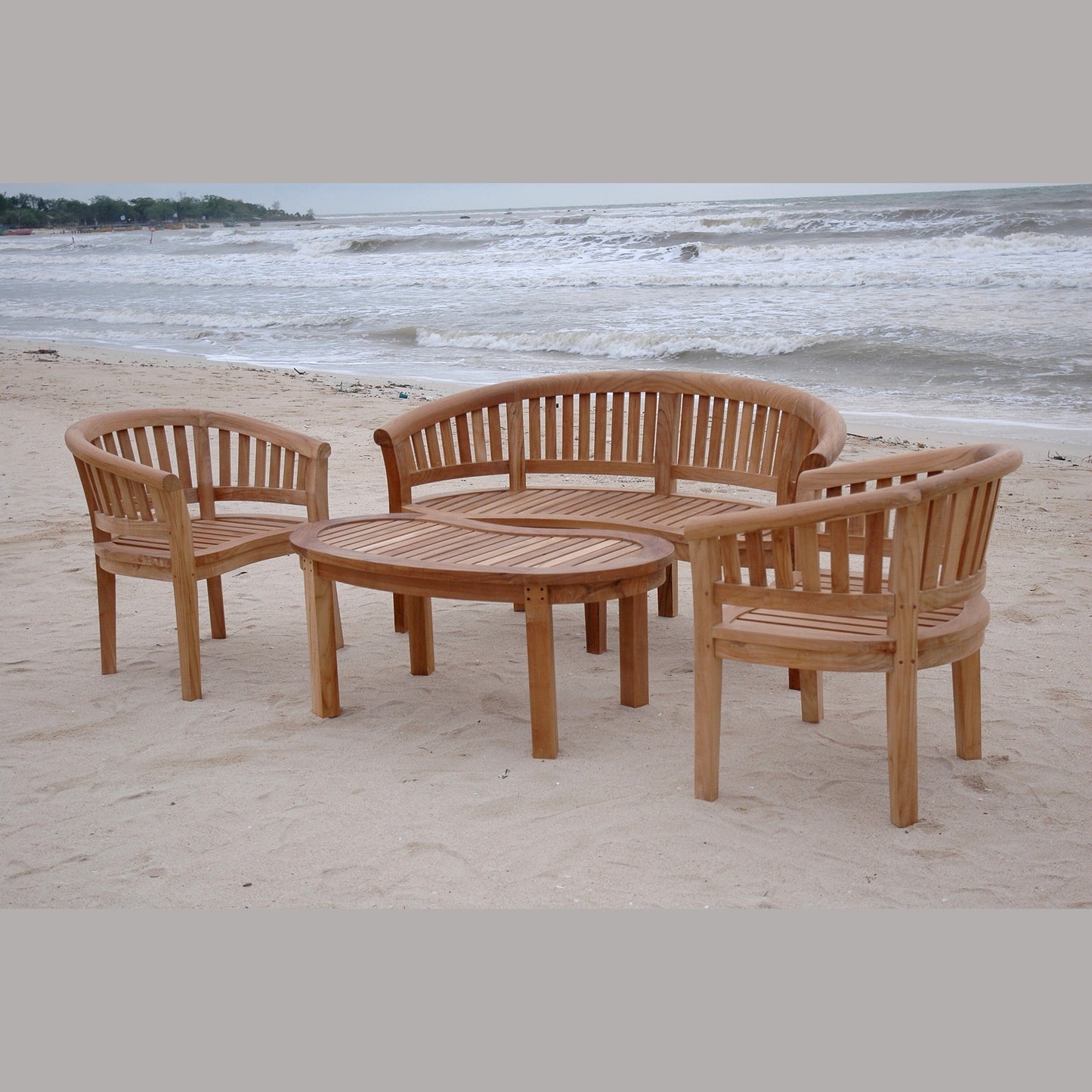 Wooden outdoor furniture set on a sandy beach with ocean waves in the background