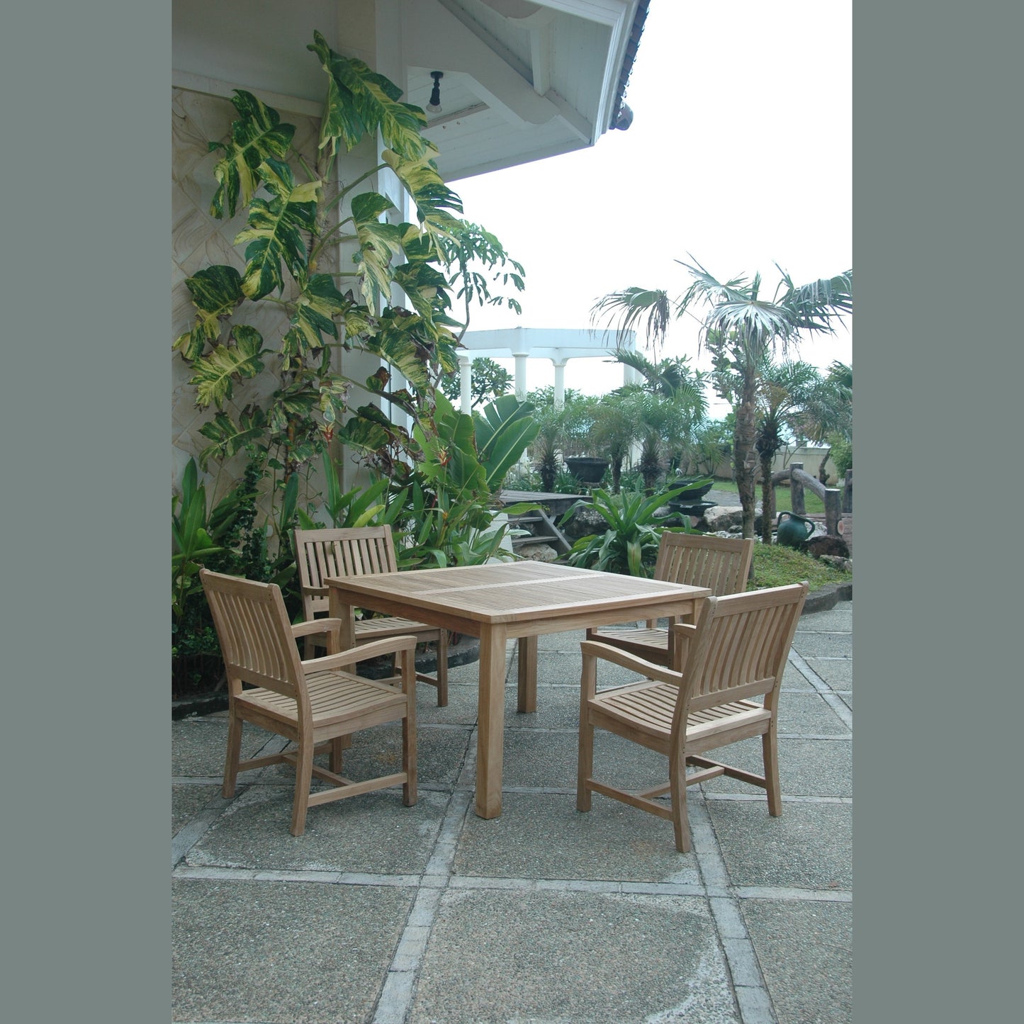 Wooden outdoor dining set with chairs on a patio surrounded by plants