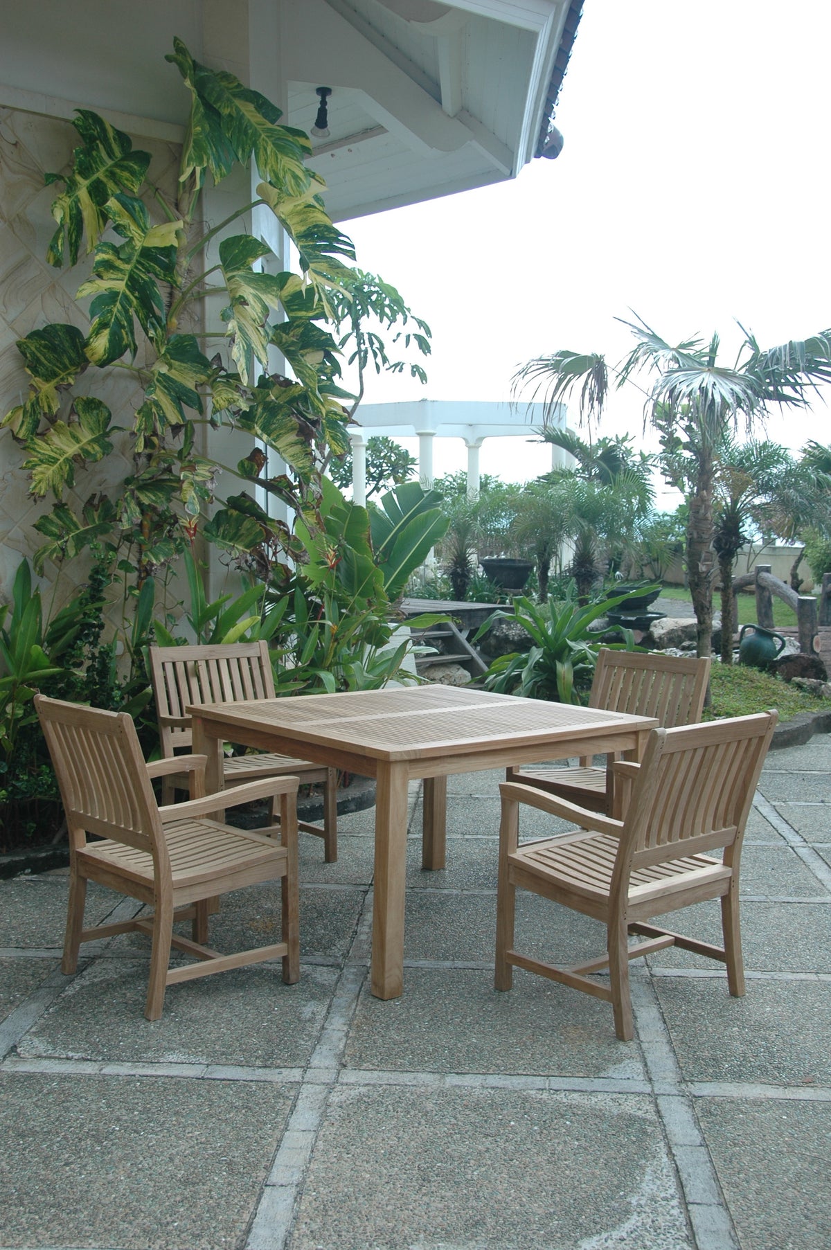 Wooden outdoor dining set with chairs on a patio surrounded by plants