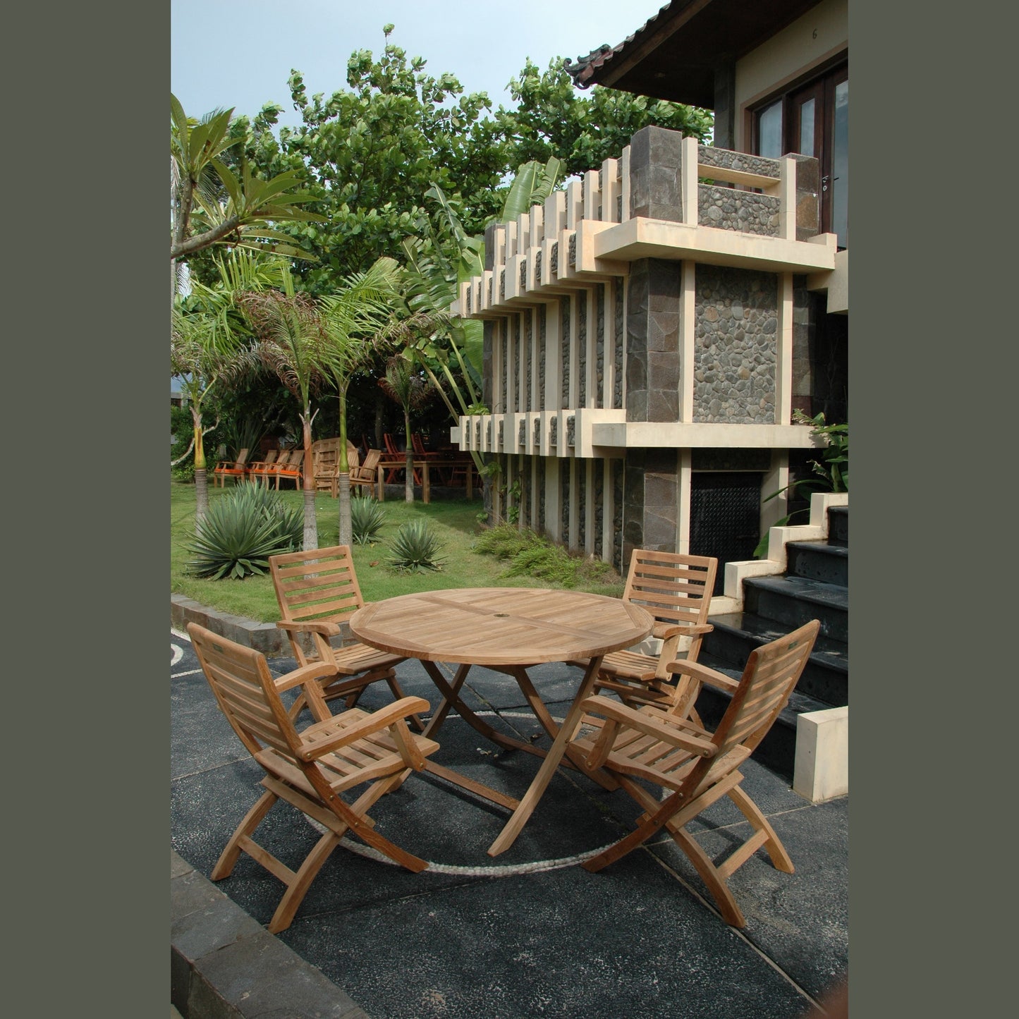 Wooden outdoor furniture set on a patio with a modern building and greenery in the background