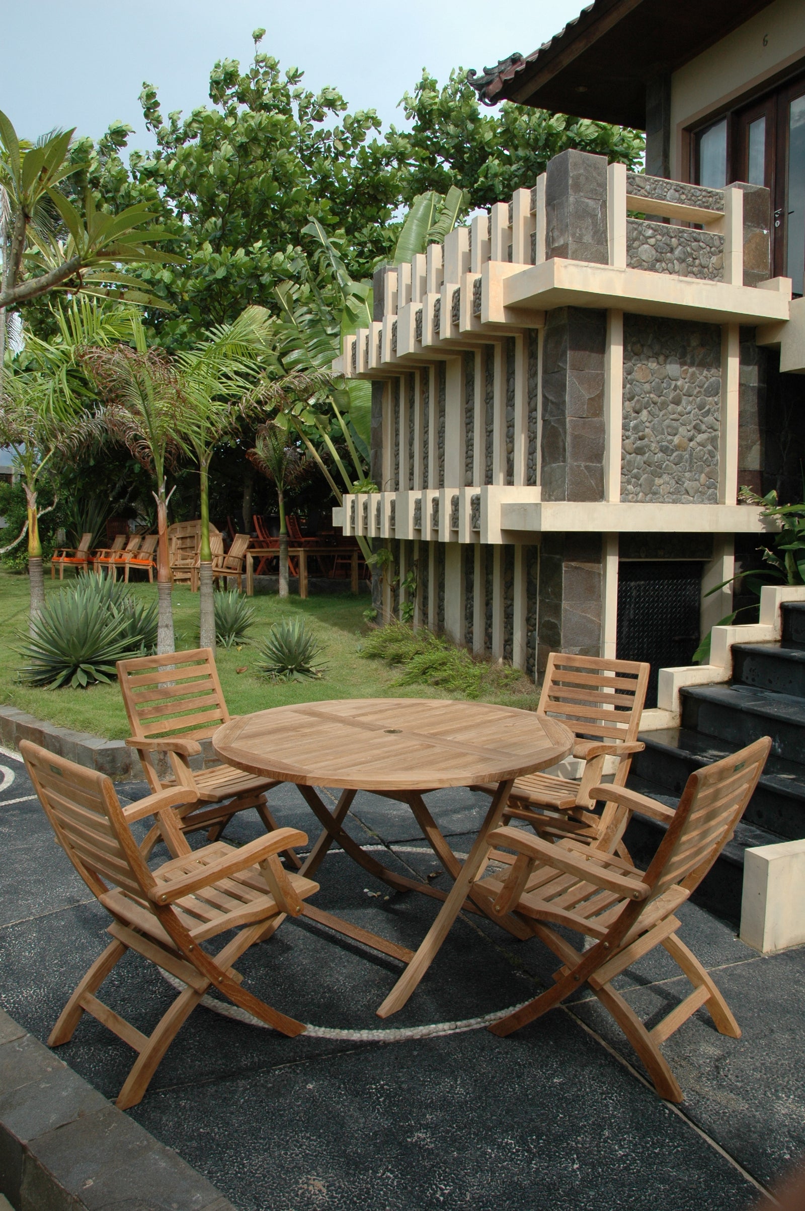Wooden outdoor furniture set on a patio with a modern building and greenery in the background