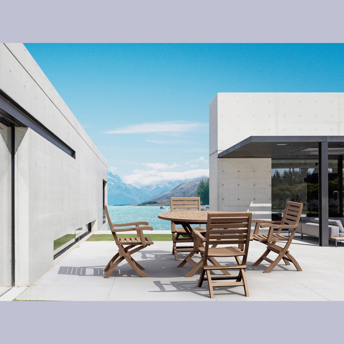 Outdoor dining area with wooden table and chairs in front of a modern house with a mountain view.