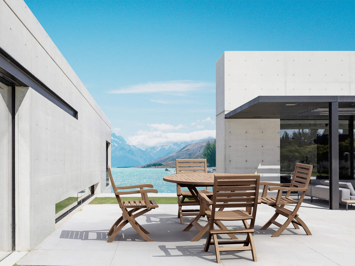 Outdoor dining area with wooden table and chairs in front of a modern house with a mountain view.