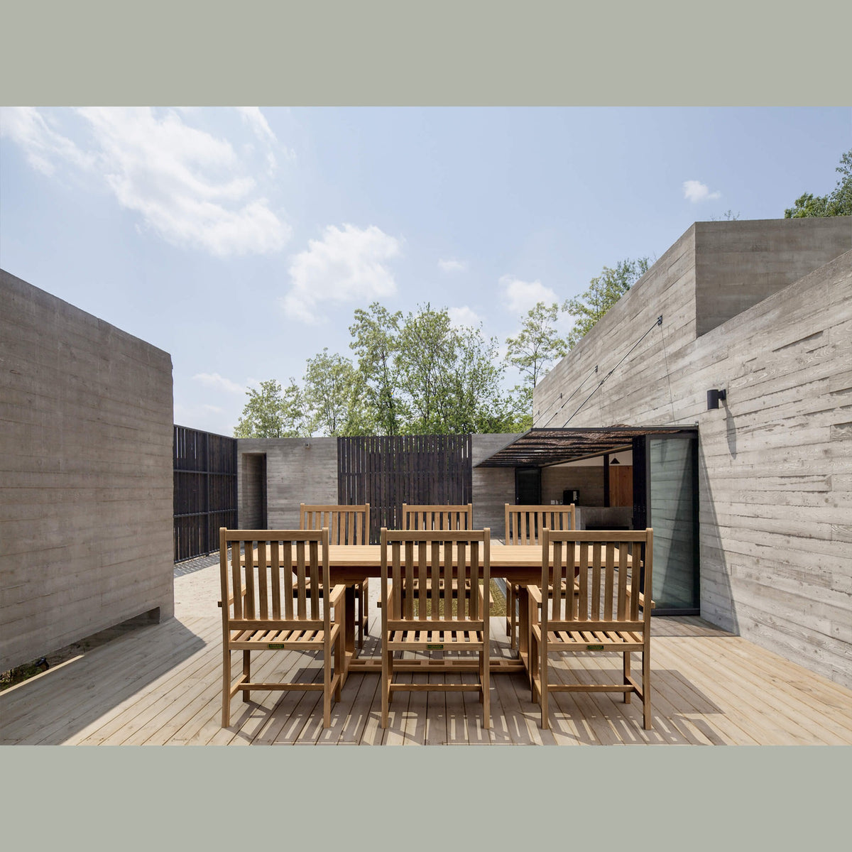 Wooden outdoor dining set in a modern architectural setting with concrete walls and a clear sky.