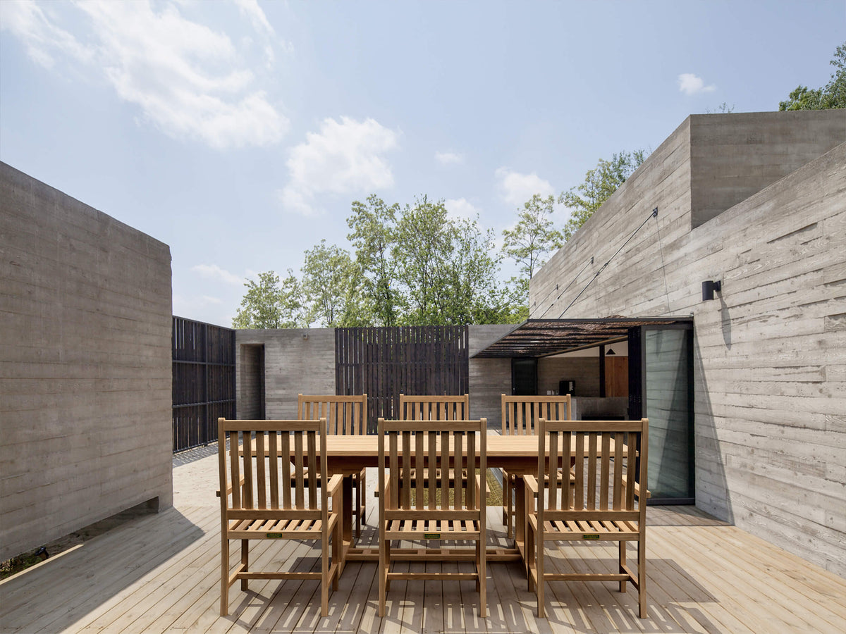 Wooden outdoor dining set in a modern architectural setting with concrete walls and a clear sky.