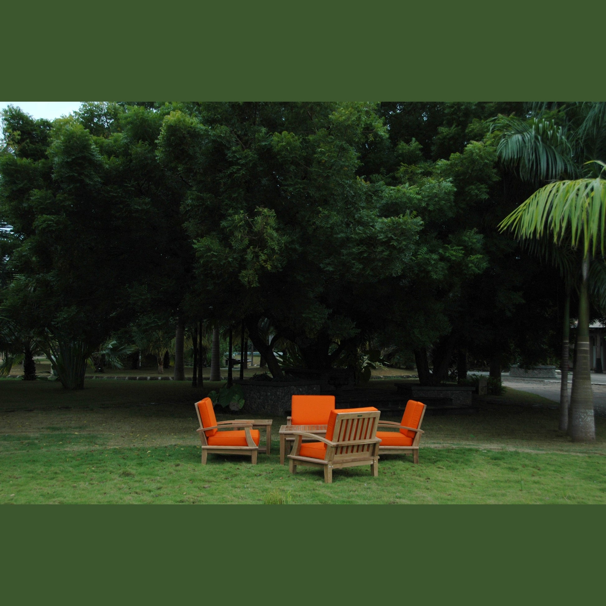 Outdoor furniture set with orange cushions under a large tree in a park.