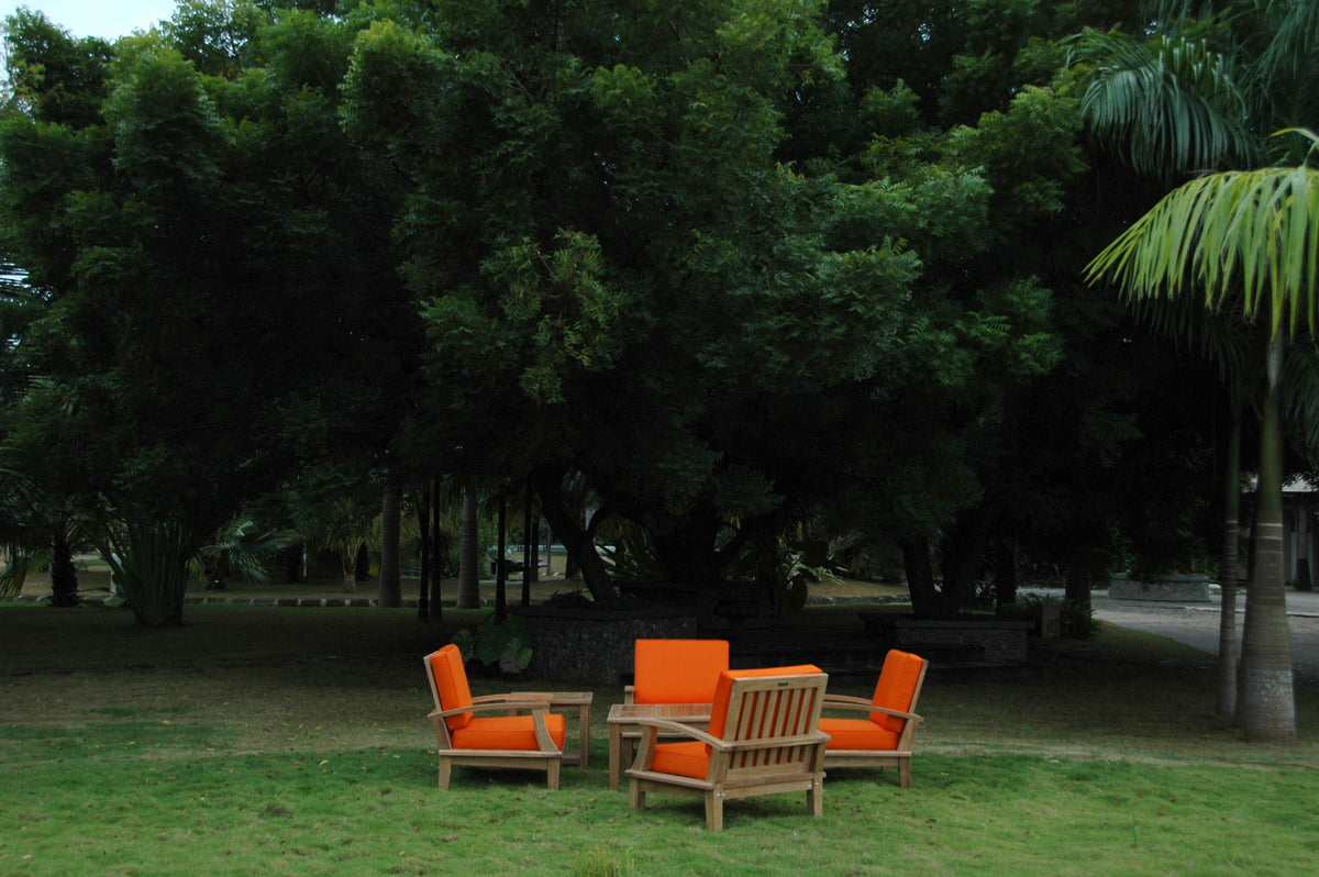 Outdoor furniture set with orange cushions under a large tree in a park.