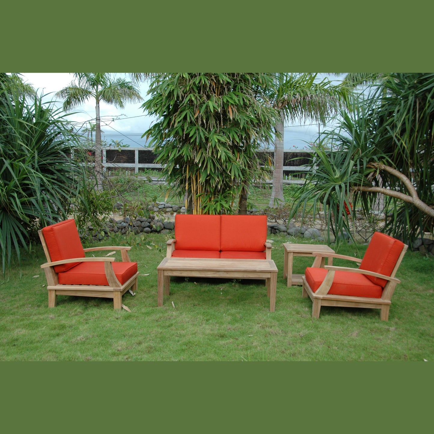 Outdoor furniture set with red cushions on a grassy area with greenery.
