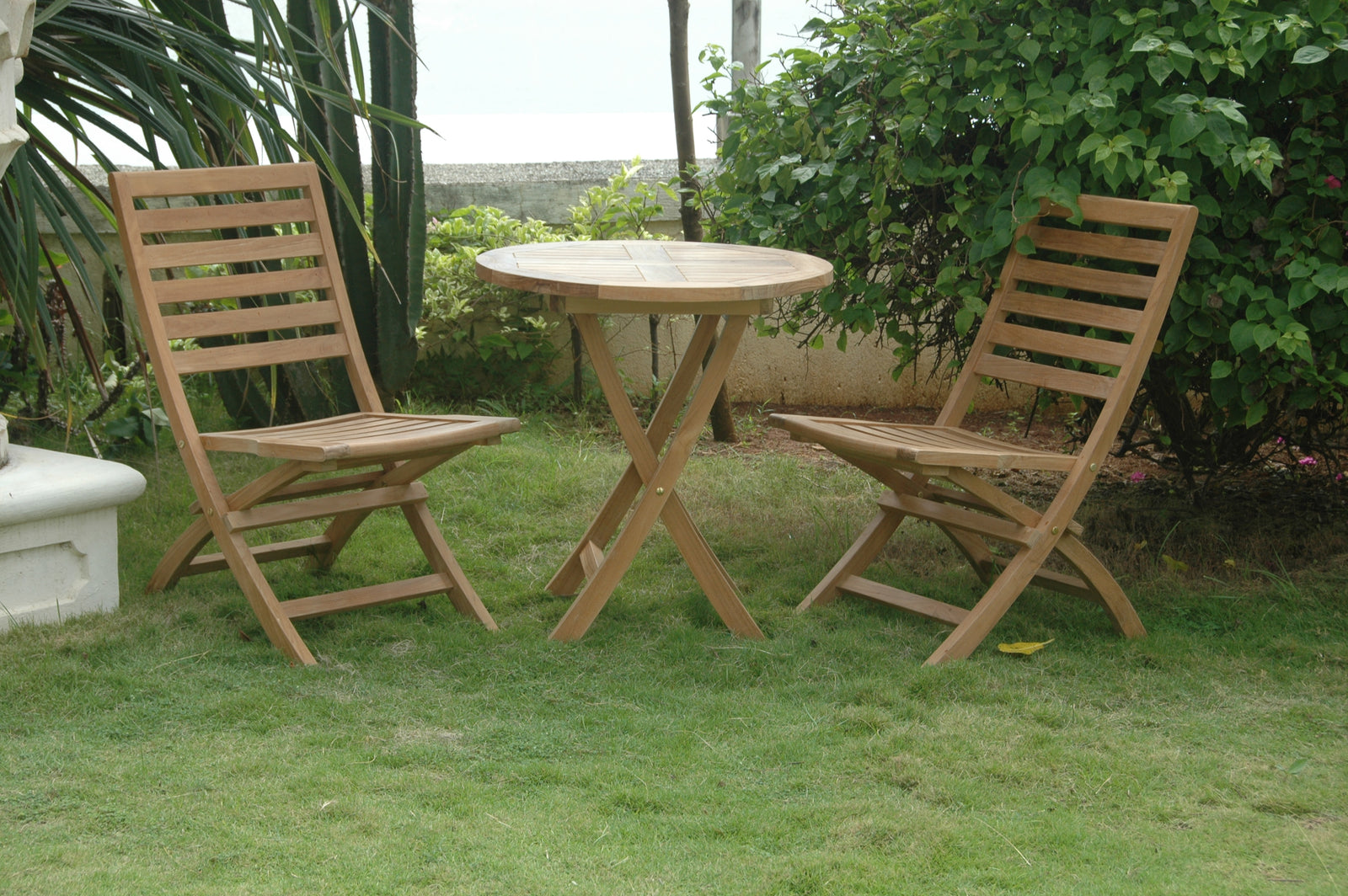 Wooden outdoor table and chairs on a grassy area with greenery in the background