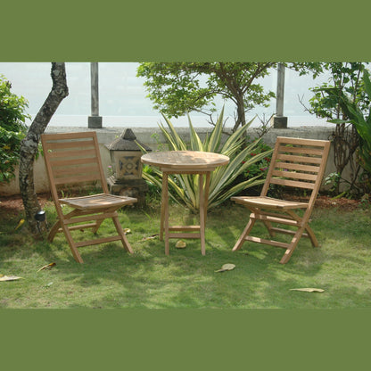 Two wooden chairs and a round table on a grassy area with plants and a wall in the background.