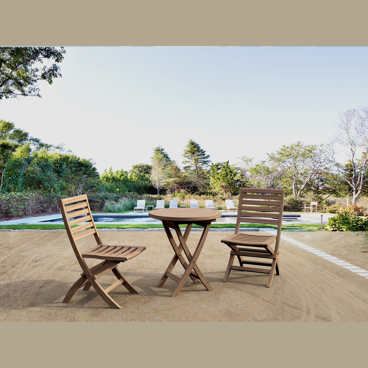 Wooden outdoor table with two chairs on a patio area with trees and a pool in the background.