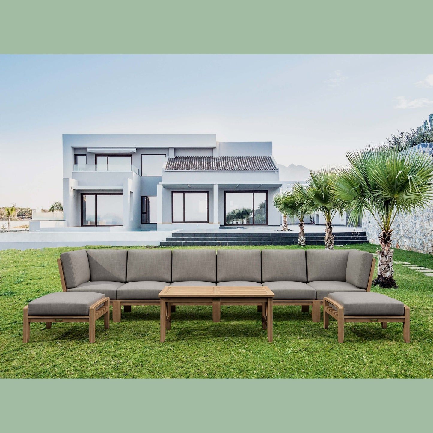 Outdoor patio furniture set with gray cushions on a grassy lawn in front of a modern house.