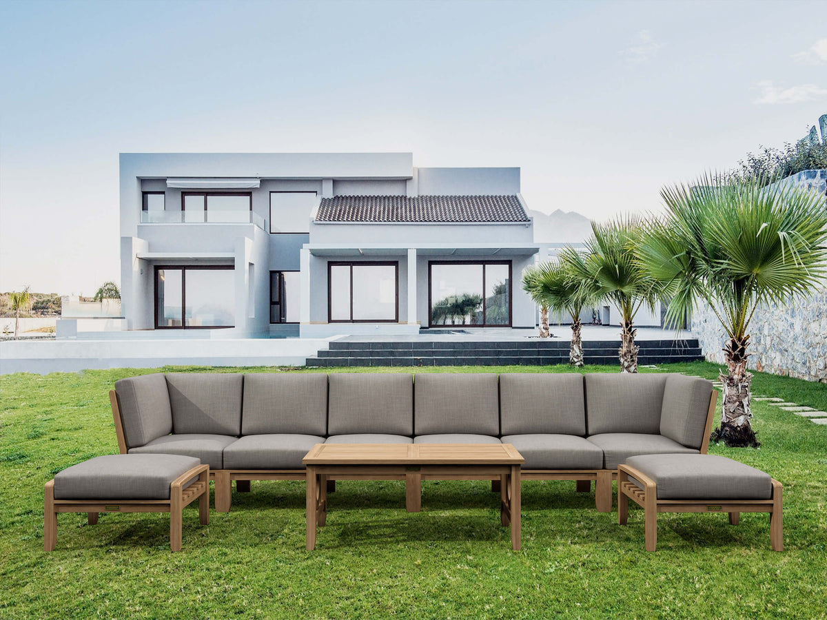 Outdoor patio furniture set with gray cushions on a grassy lawn in front of a modern house.