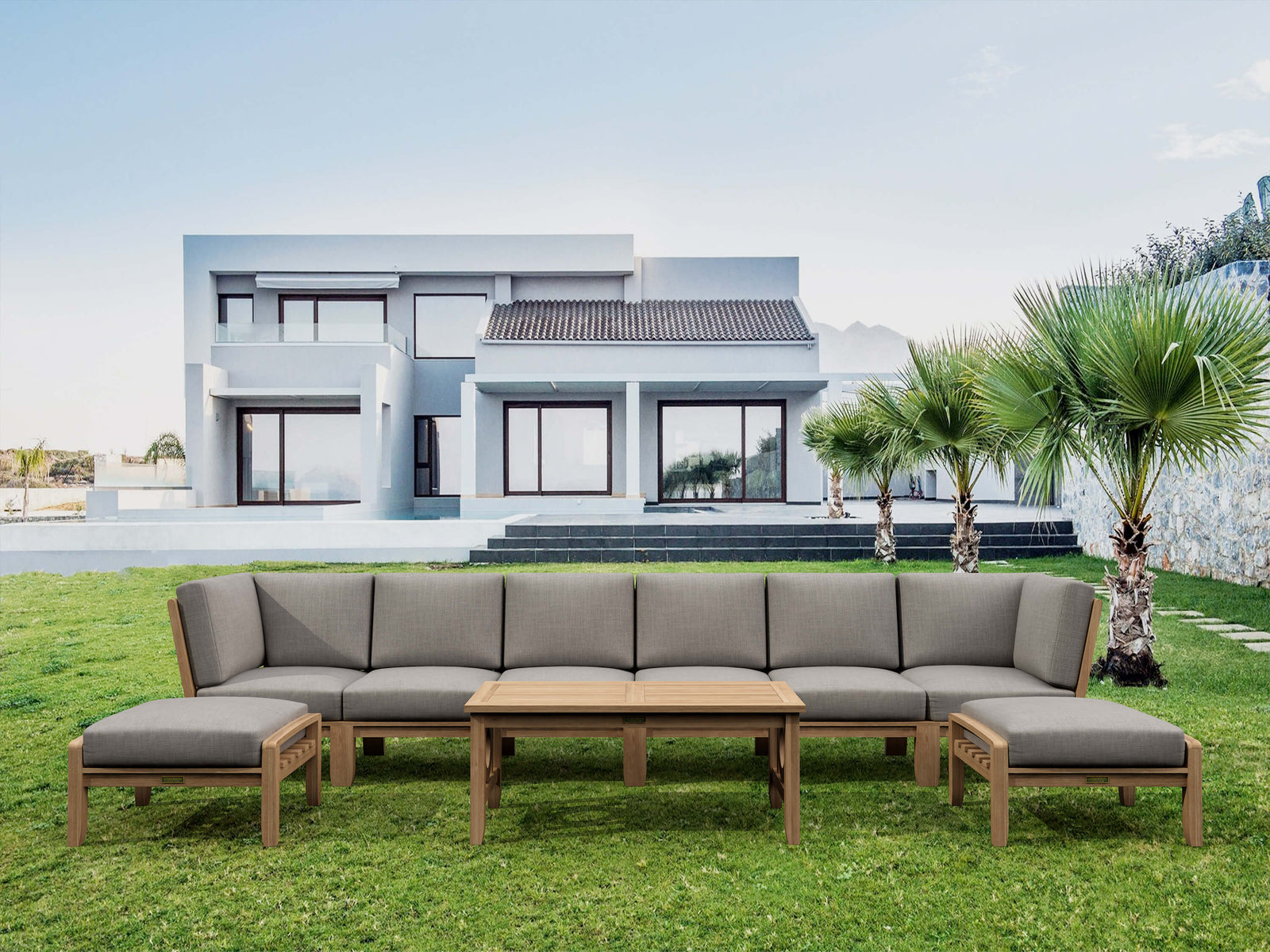 Outdoor patio furniture set with gray cushions on a grassy lawn in front of a modern house.
