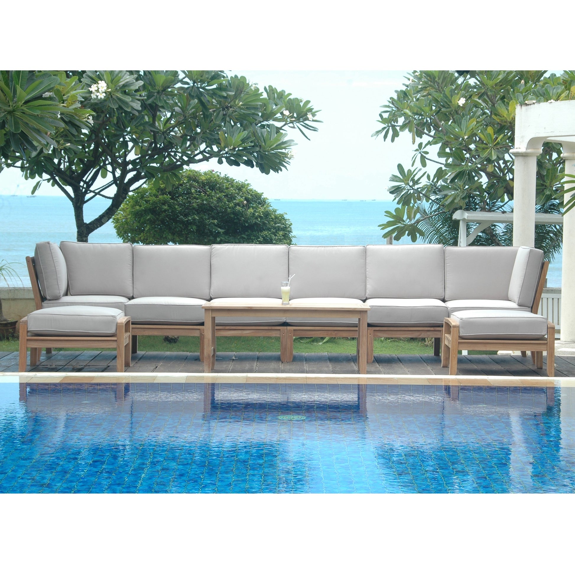 Outdoor patio sectional with beige cushions by a poolside with ocean view