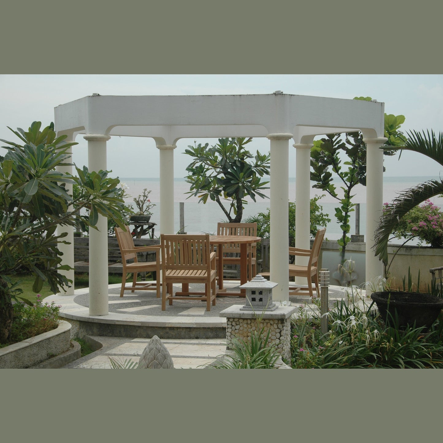 Patio with wooden furniture under a white pergola surrounded by greenery.