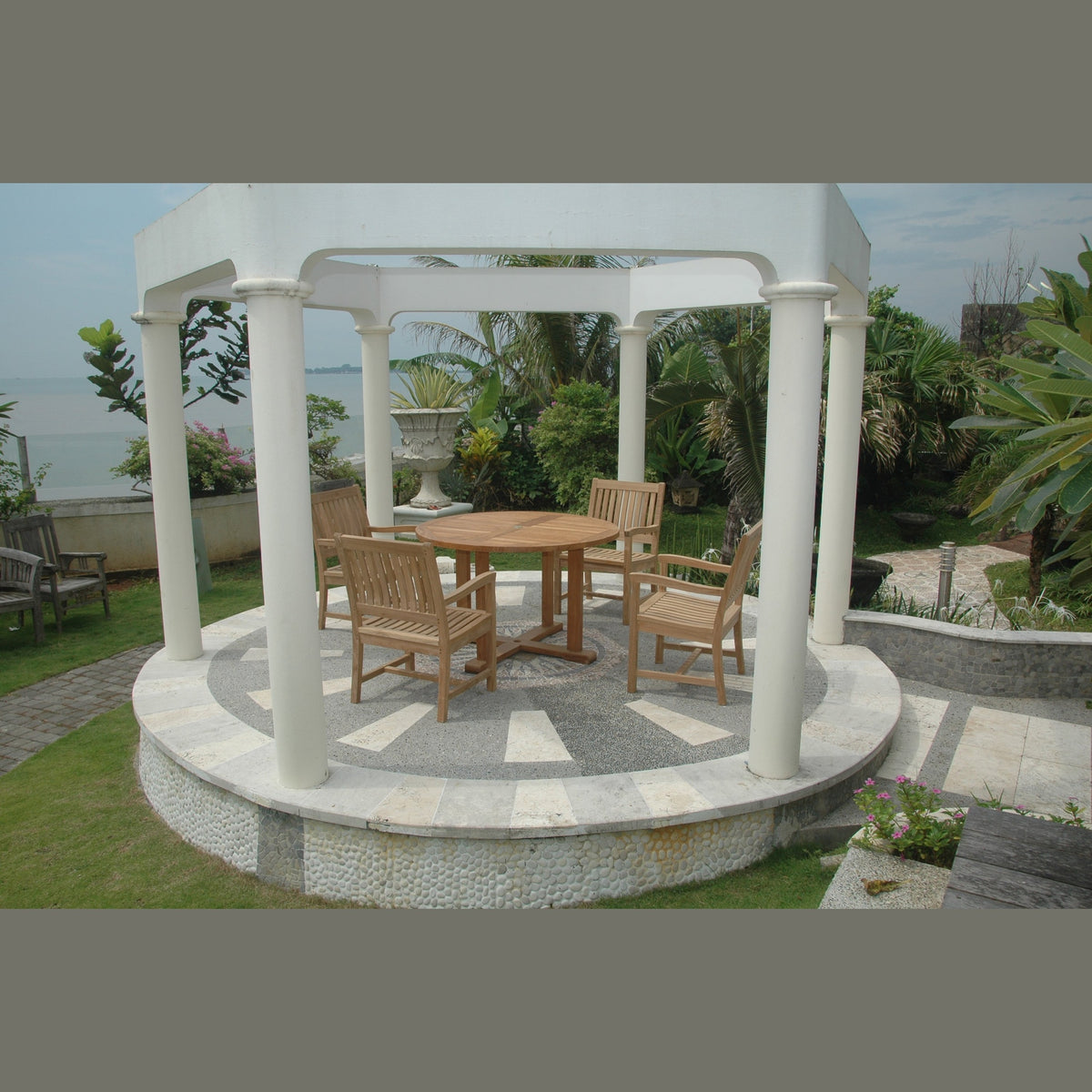Gazebo with wooden furniture on a patio area by a body of water.