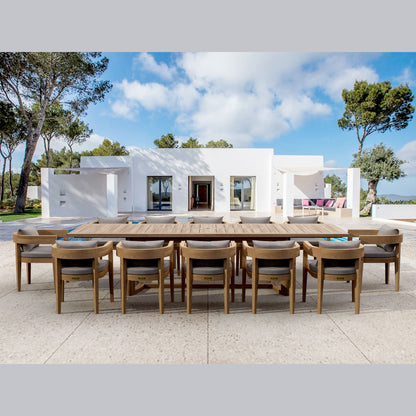 Outdoor dining area with a large wooden table and chairs in front of a modern white house.