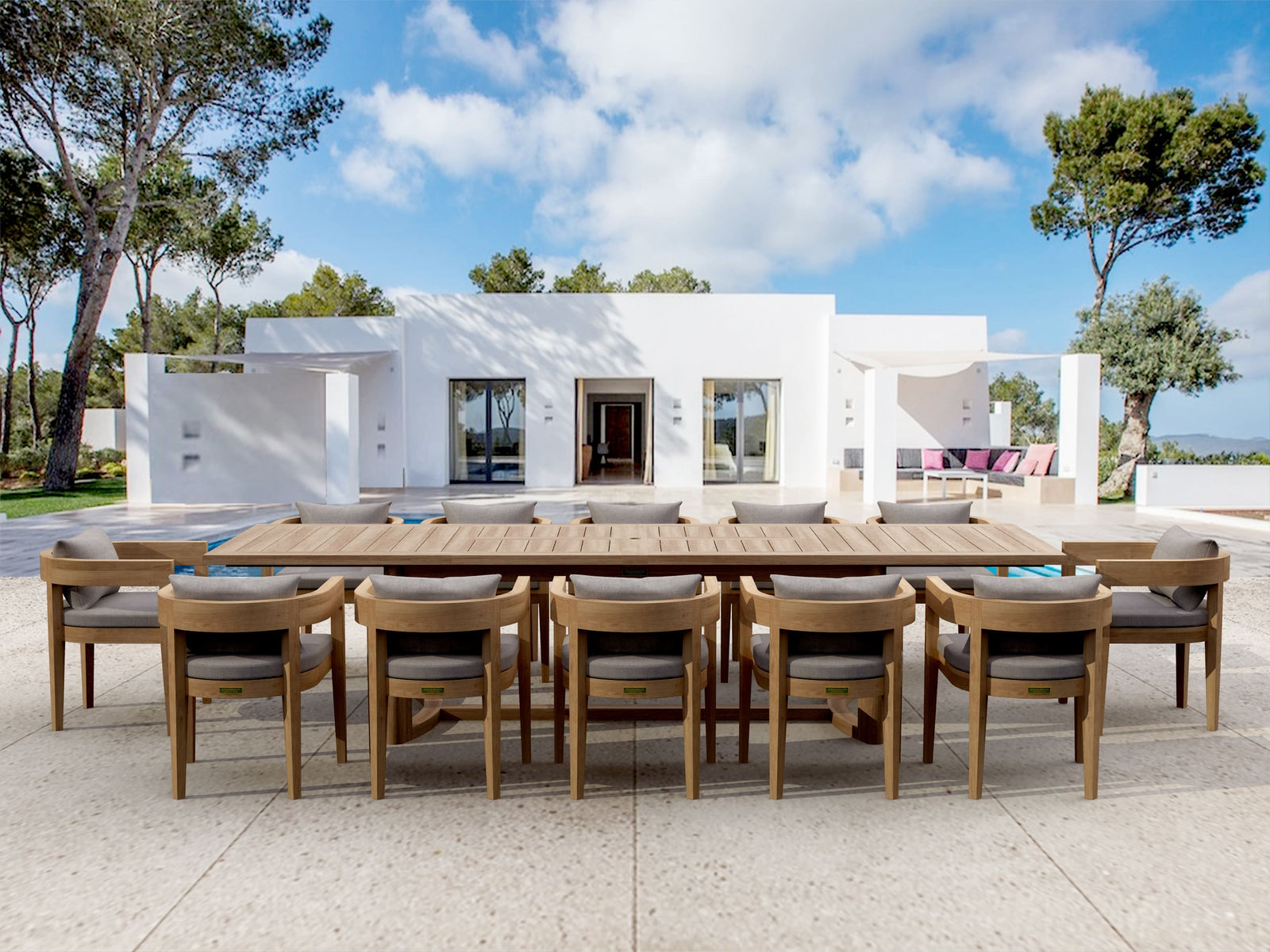 Outdoor dining area with a large wooden table and chairs in front of a modern white house.