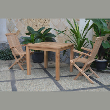 Wooden outdoor table with two chairs on a stone patio surrounded by plants.