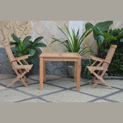 Wooden table with two chairs on a patio with plants and stone wall in the background
