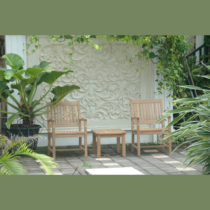 Two wooden chairs and a small table on a patio with decorative wall and plants.