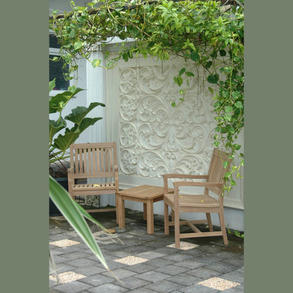 Two wooden chairs and a table under a green archway with a decorative wall in the background.