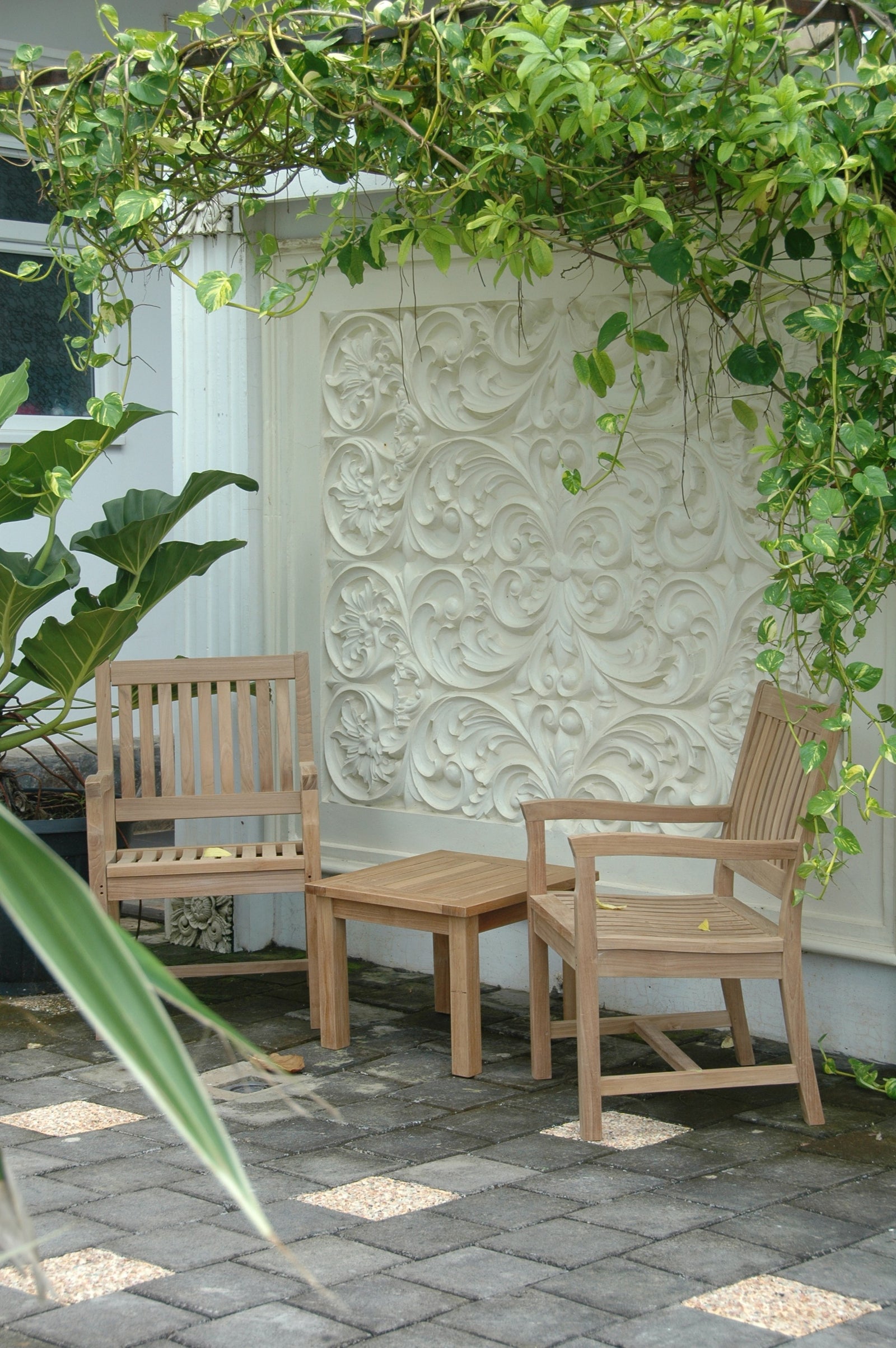 Two wooden chairs and a table under a green archway with a decorative wall in the background.