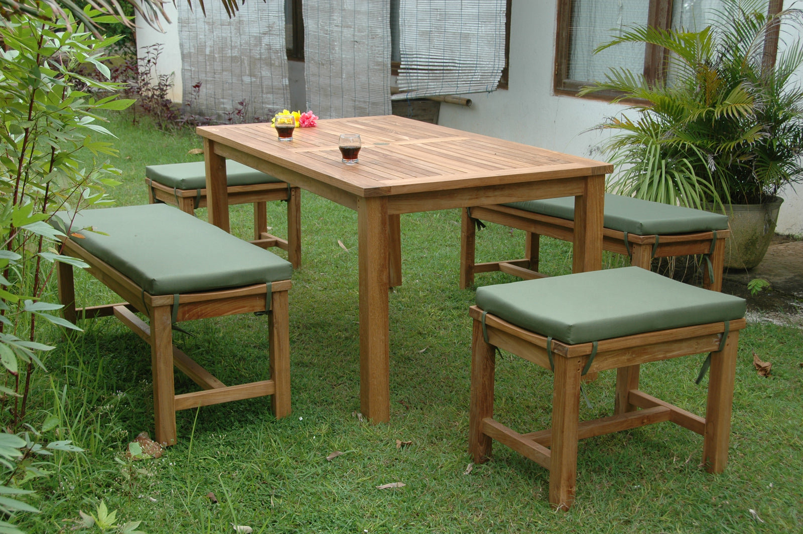 Wooden outdoor dining set with green cushions on a grassy area.