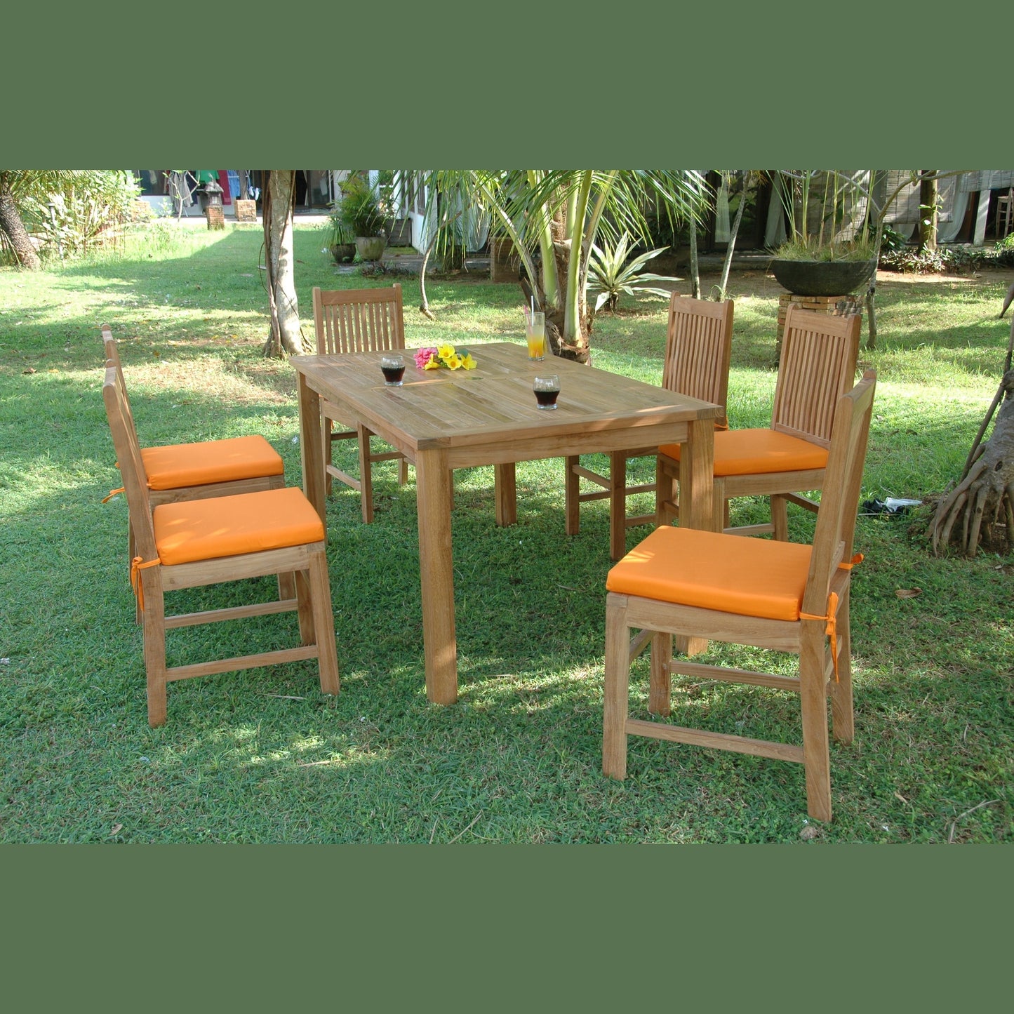 Wooden dining table with four chairs and orange cushions on a grassy area